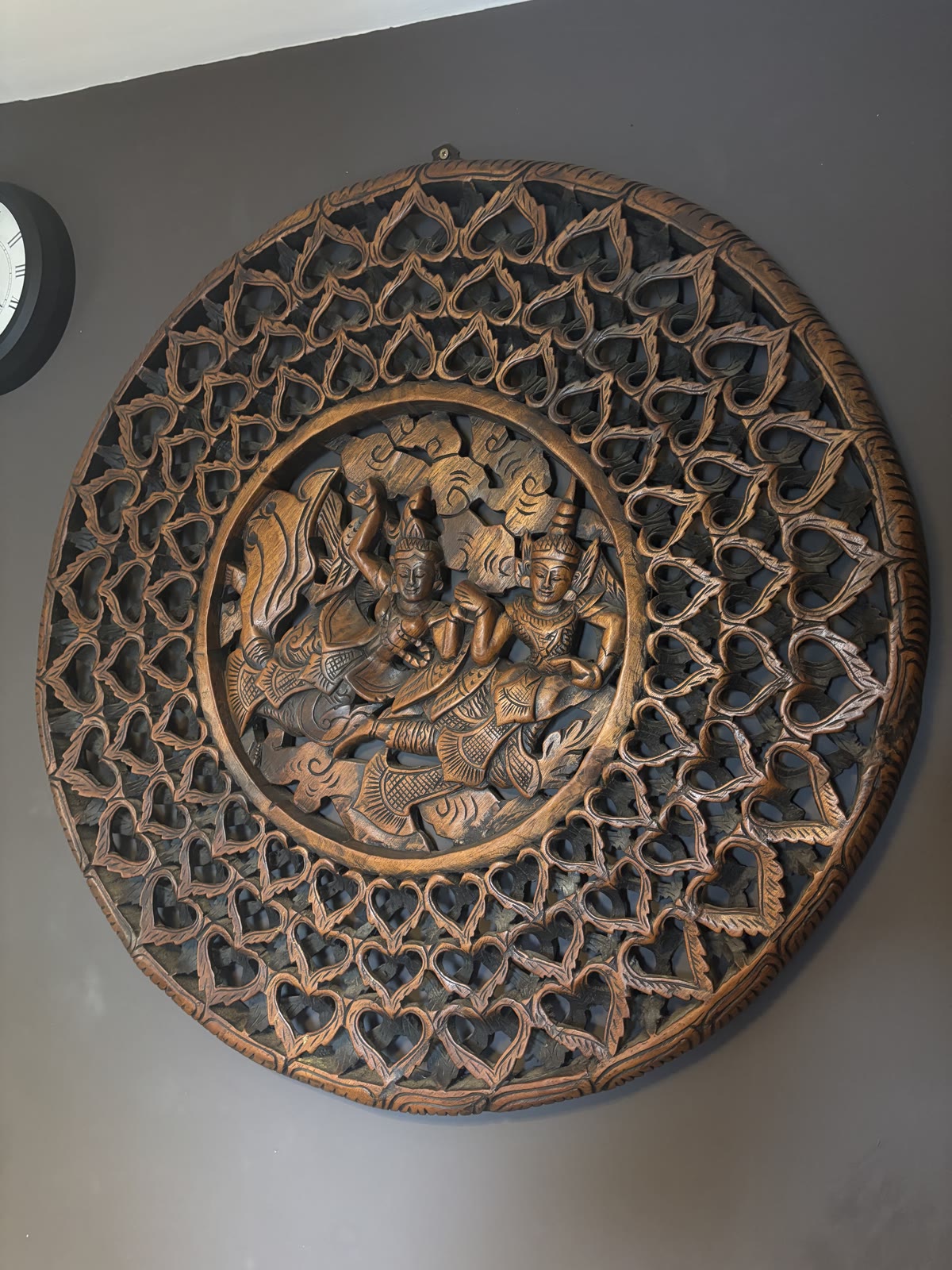 A large circular hand-carved Thai wood medallion depicting two dancing figures